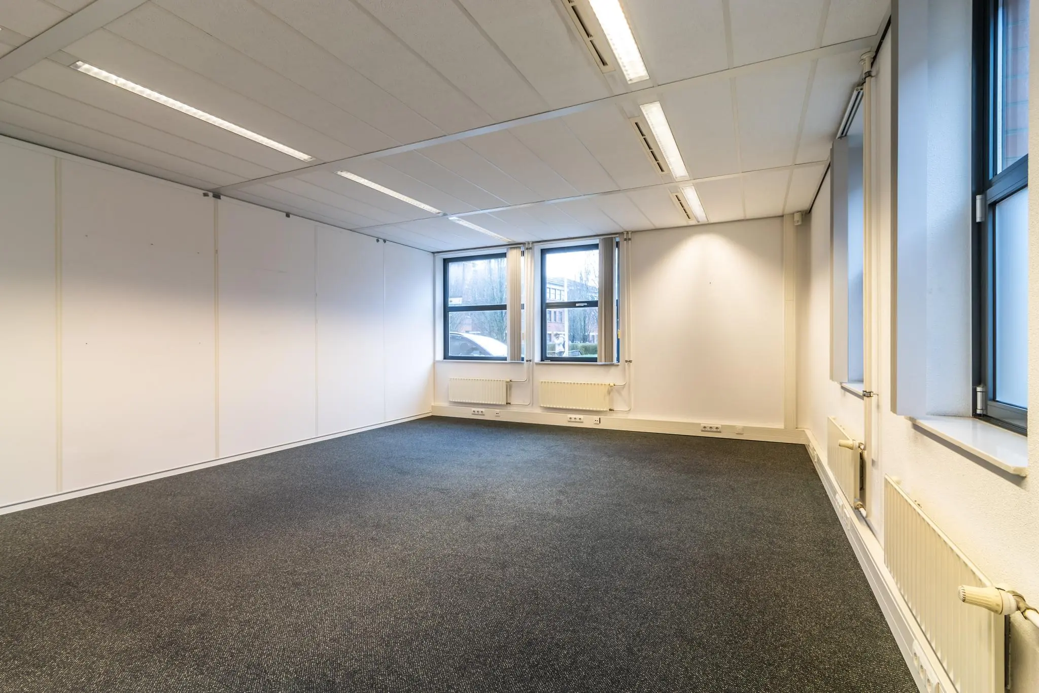 Leeg kantoorruimte aan de Lange Dreef met tapijtvloer, systeemplafond en ramen aan twee zijden.